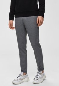 Pantaloni jogger grigi in tessuto morbido, caratterizzati da una vestibilità slim e un design affusolato. Abbinati a sneaker bianche e grigie.