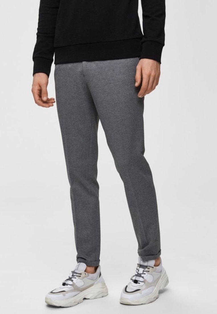 Pantaloni jogger grigi in tessuto morbido, caratterizzati da una vestibilità slim e un design affusolato. Abbinati a sneaker bianche e grigie.