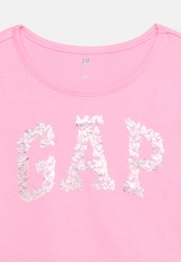 Ροζ παιδικό μπλουζάκι με το γράμμα "GAP" σχηματισμένο από ασημένιες πεταλούδες στο μπροστινό μέρος και στρογγυλή λαιμόκοψη.