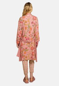 Roze kimono met bloemenpatroon en lange mouwen, met een gestrikte taille; gecombineerd met muntgroene broek met een geometrisch ontwerp; zachte textuur.