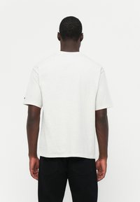 Light gray cotton t-shirt, relaxed fit with short sleeves, round neckline, and minimal stitching details, viewed from the back.