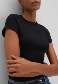 Zwarte ribgebreide korte mouwen t-shirt, getailleerde pasvorm, ronde halslijn, gladde textuur, gedragen met denim jeans en een zwarte riem.