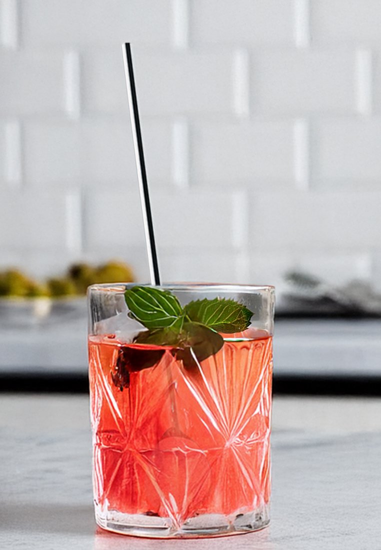 Przezroczysty szklany kubek wypełniony różowym napojem, lodem i liśćmi mięty; posiada teksturowany wzór i czarną słomkę.