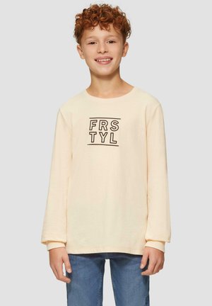Cremefarbendes Langarmshirt mit rundem Halsausschnitt, das den Text "FRSTYL" in Schwarz trägt. Kombiniert mit blauen Denim-Jeans. Aus weichem Baumwollmaterial.