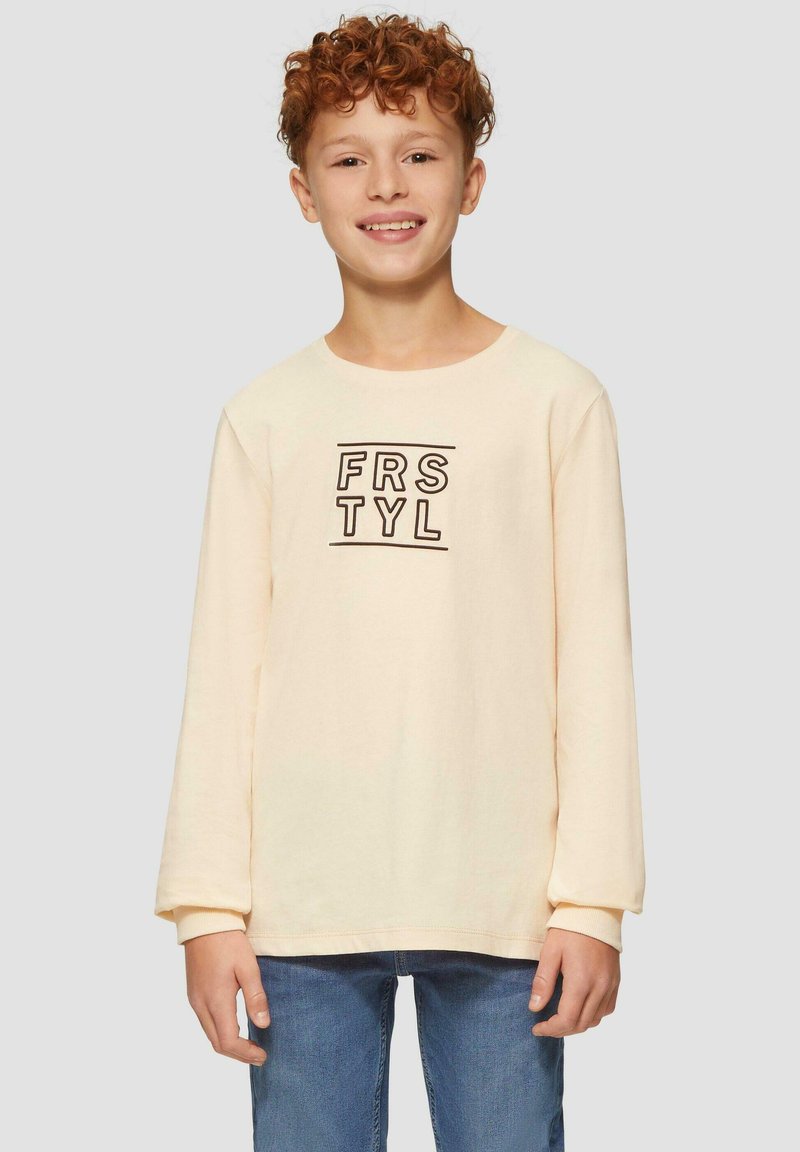 Cremefarbendes Langarmshirt mit rundem Halsausschnitt, das den Text "FRSTYL" in Schwarz trägt. Kombiniert mit blauen Denim-Jeans. Aus weichem Baumwollmaterial.