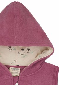 Fleece capuchon kledingstuk in zacht paarse wol, met een beige voering met zwarte schapenillustraties en groene grassaccenten. Ritsluiting.
