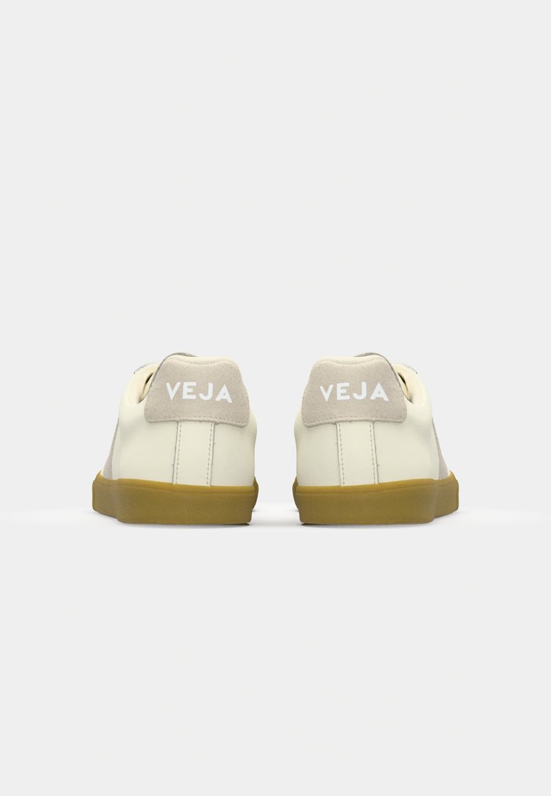Baskets en cuir blanc avec des accents beiges et une semelle en caoutchouc. Présentent le logo 'VEJA' sur le talon et une texture lisse. Design simple.
