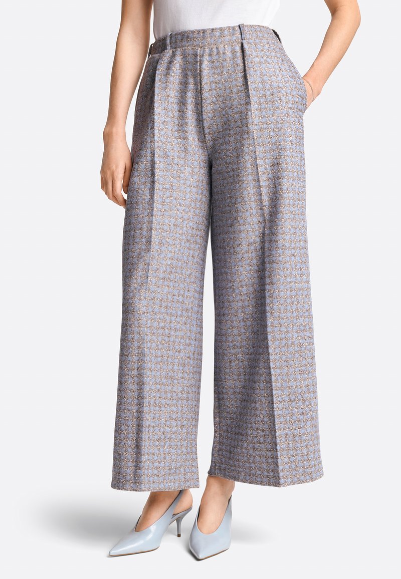 Wide-leg trousers in a blue fabric with a delicate pattern. Features a high waist, pleats, and side pockets. Paired with light blue heels.