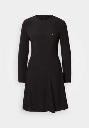 Black long-sleeve dress with a round neckline and slight A-line shape. Features a discreet logo on the chest and textured fabric accents at the sleeves.