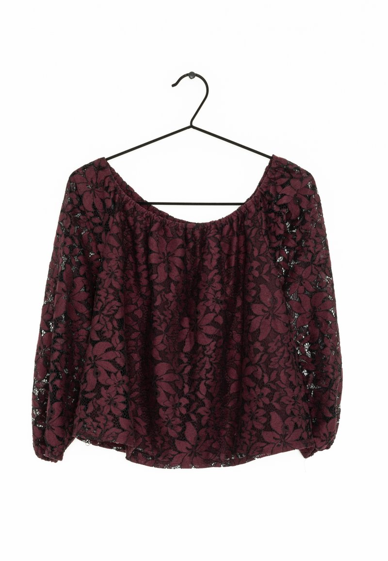 Burgundy topp med ett blommigt spetsmönster, lös passform, off-shoulder-design och långa ärmar. Hänger från en svart metallkrok.