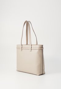 Sac fourre-tout en cuir beige avec deux longues poignées, une forme rectangulaire élégante, et des accents cloutés discrets le long du bord supérieur.