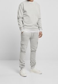 Felpa grigia chiara e pantaloni cargo abbinati realizzati in tessuto morbido. La felpa ha maniche a costine; i pantaloni presentano tasche cargo e una vita con coulisse.