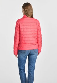 Różowa pikowana kurtka z wysokim kołnierzem i poziomym szyciem, w połączeniu z niebieskimi dżinsami. Tekstura wydaje się gładka, a kurtka ma dopasowany krój.