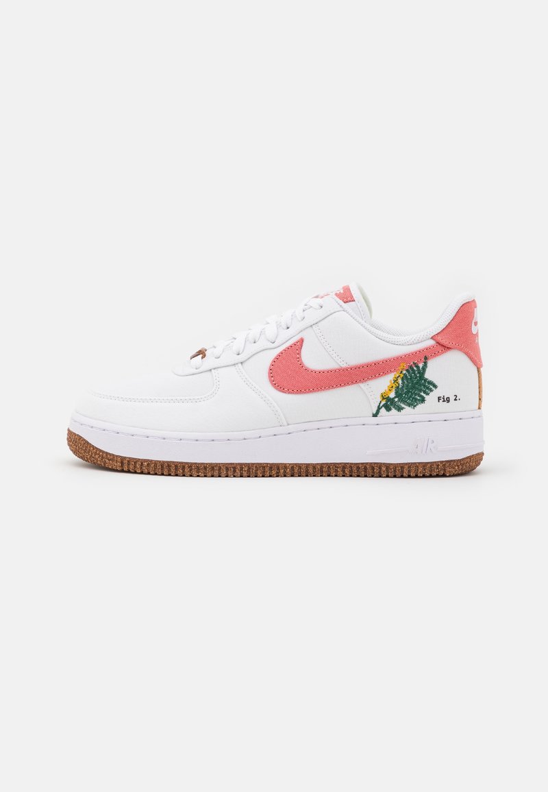 Baskets blanches Nike Air Force 1 avec le logo Swoosh rose, broderies florales vertes et jaunes, et semelle en caoutchouc marron sur un fond uni.