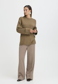 Suéter de punto marrón con cuello redondo, ajuste holgado y puños acanalados, combinado con pantalones de pierna ancha beige y calzado oscuro.