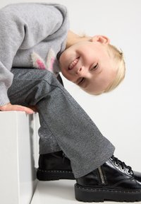 Suéter cinzento com desenho de coelho rosa, combinado com calças cinzentas brilhantes e botas pretas com atacadores, fecho lateral e sola texturada.