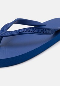 Plave gumene japanke s teksturiranim uloškom i glatkim trakama. Na traci je utisnut logo "JACK & JONES". Dizajn s okruglim prstima.