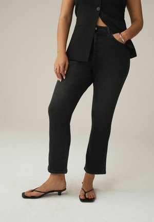 Persona con blazer negro sin mangas, vaqueros rectos de tiro alto negros, sandalias negras de tacón bajo con tiras y joyas plateadas.