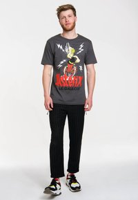 Gray short-sleeve t-shirt featuring a colorful Asterix graphic, paired with black pinstriped pants and multicolored sneakers.