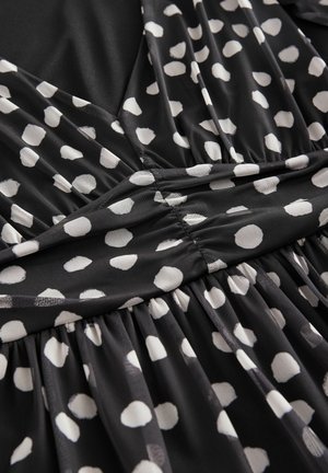 Melnas auduma kleita ar polka dot paraugu, kuram ir baltas punktiņi. Materiāls ir mīksts un viegls, ar savākšanas detaļām jostasvietā.