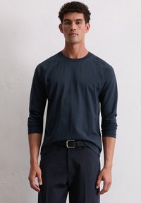 Navy lange mouwen crewneck shirt met raglan mouwen, gemaakt van zachte stof. Draag het met een zwarte riem, in combinatie met donkere broek.