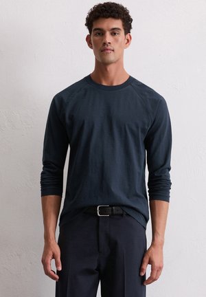 Navy lange mouwen crewneck shirt met raglan mouwen, gemaakt van zachte stof. Draag het met een zwarte riem, in combinatie met donkere broek.