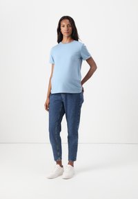 Tricou din bumbac de culoare bleu deschis, cu mâneci scurte și decolteu rotund, asociat cu blugi din denim tapered și adidași albi. Design și croială simple.