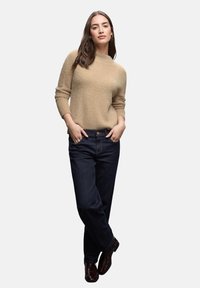 Beige, mjuk, texturerad tröja med trekvartslånga ärmar, i kombination med mörkblå, avslappnade jeans och mörkbruna ankelstövlar.