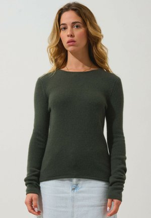 Maglione a maniche lunghe di colore verde scuro con scollatura tonda e tessuto a costine, abbinato a una gonna di jeans chiaro.