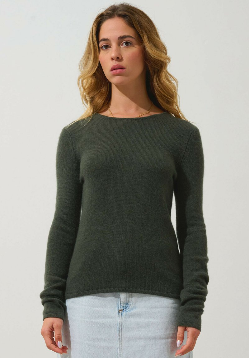 Donkergroen, gebreid sweater met lange mouwen, ronde hals en ribbelstructuur, gedragen met een lichte spijkerrok.