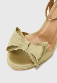Gullsatin høyhælte sandal med en stor sløyfe på forsiden, åpen tå-design og en glatt beige innersåle.
