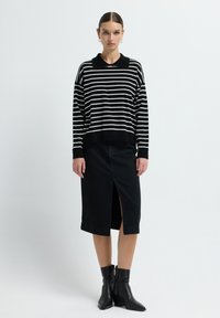Maglione a righe bianche e nere con colletto, abbinato a una gonna midi nera con spacco frontale, indossato con stivali neri alla caviglia.