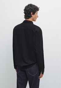 Schwarzes Cordhemd mit Button-Down-Kragen, langen Ärmeln und lockerer Passform. Verfügt über einen strukturierten Stoff und klassische Knopfmanschetten-Details.