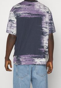 Grafické tričko s námořnickou základnou a abstraktními fialovými a bílými štětcovými tahy, krátké rukávy a kulatý výstřih.