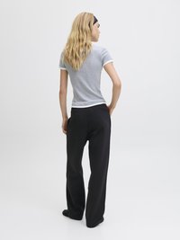 Grå kortermet t-skjorte med hvit kant, kombinert med løse svarte joggebukser; enkelt design og glatt stoff. Modell vender bort fra kameraet.