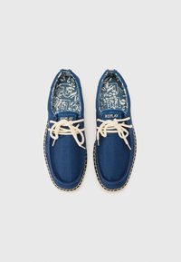 Chaussures en tissu tissé bleu avec des lacets blancs, une semelle cousue de couleur claire et un intérieur à motifs présentant des designs floraux. Étiquette de la marque "REPLAY."