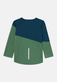 Camisa de manga larga en azul marino y verde. Presenta un diseño a bloques de color, dobladillo redondeado y una franja reflectante en la parte posterior. Textura suave.