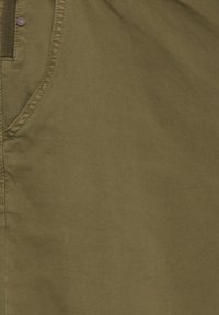 Olivově zelený panel z tkaniny, směs bavlny, s hladkou texturou, viditelným šitím a měděně zbarveným knoflíkem u okraje.