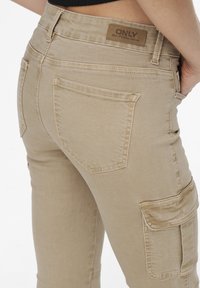 Beiga cargobyxor med smal passform, två bakfickor och en slät denimtextur. En brun läderetikett med "ONLY" är synlig vid midjan.