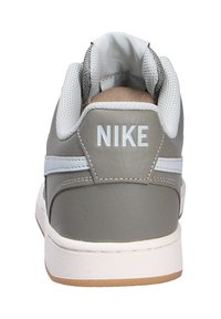 Las zapatillas Nike de cuero gris tienen un talón acolchado, acentos blancos y una lengua texturizada. La suela de goma es de color marrón claro y plana.