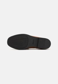 Suela de zapato de cuero marrón con una suela exterior de caucho negro texturizado que presenta perforaciones para transpirabilidad y un diseño de borde liso.