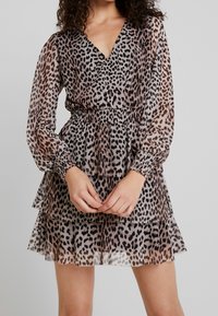 Leopardmönstrad chiffongklänning med långa ärmar, V-ringning, smockad midja och lagerkjol. Färgerna inkluderar beige, svart och brunt.