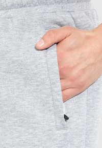 Pantalones de chándal grises con una textura suave, que cuentan con un bolsillo lateral y un pequeño cordón negro. La tela parece suave y casual.