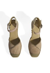 Sandales en suède beige avec des brides croisées, fermeture à boucle à la cheville et semelle en jute tressé. Accents métalliques le long du bord de la bride.