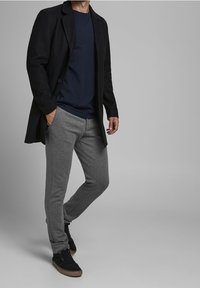 Černý sakovaný kabát, námořnické tričko, šedé tepláky a černé tenisky s hnědými akcenty. Hladký materiál s uvolněným střihem.