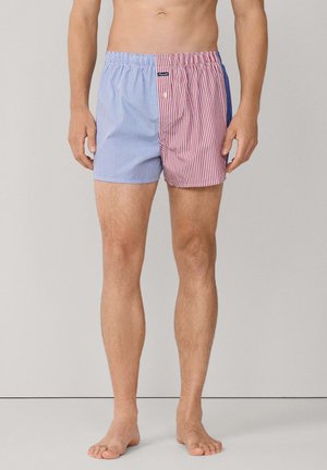 Bañador de hombre con diseño dividido, tela a rayas azules en un lado y tela a rayas rojas en el otro, cintura elástica, longitud hasta la mitad del muslo.