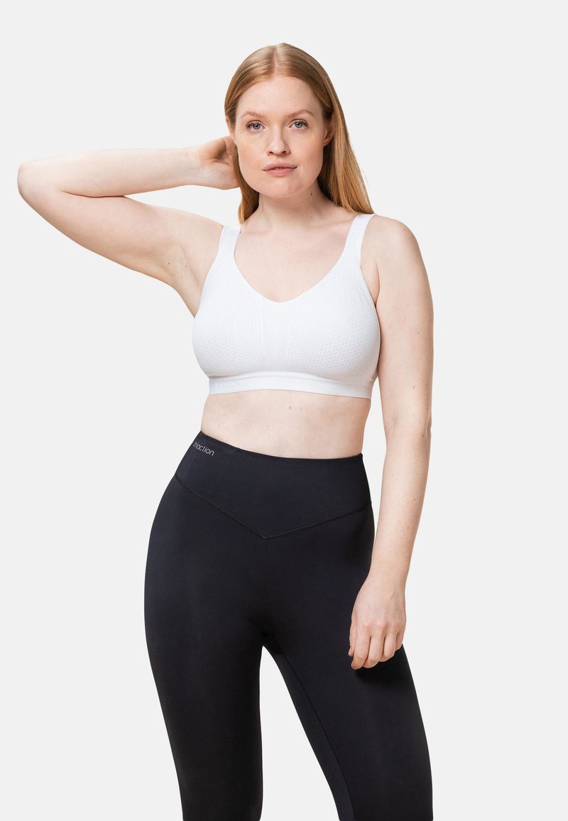 Reggiseno sportivo bianco con tessuto strutturato, spalline larghe e fascia liscia, abbinato a leggings neri a vita alta con dettaglio logo.