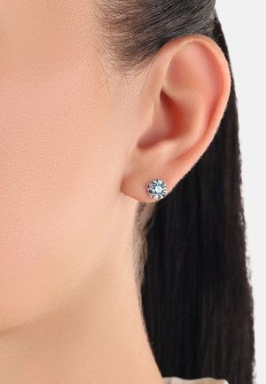 Runde, hellblaue Ohrstecker aus Silbermetall, die am Ohr eines Modells getragen werden. Sie heben die Klarheit des Edelsteins und die glatte Oberfläche hervor.