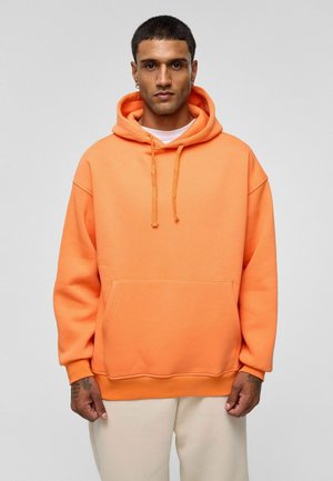 Oranje hoodie van zacht materiaal, met een voorzak, koordjes en een relaxte pasvorm met afhangende schouders.