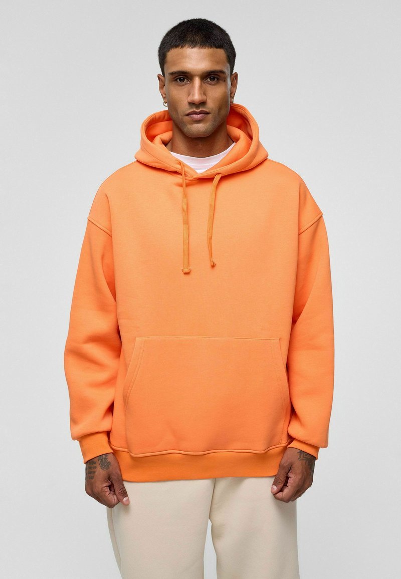 Oranje hoodie van zacht materiaal, met een voorzak, koordjes en een relaxte pasvorm met afhangende schouders.
